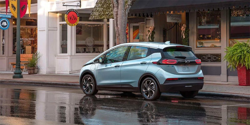 Chevy Bolt EV driving past storefronts on a wet city street