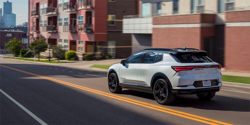 A 2025 Chevrolet Equinox EV drives along a bustling city street, showcasing its sleek design and electric capabilities.