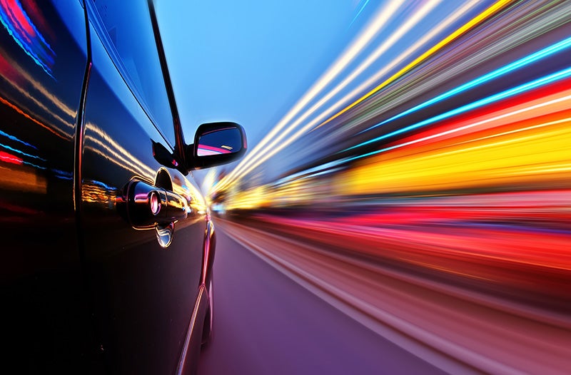 A car drives down a road, with surrounding lights appearing as colorful blurs in motion.