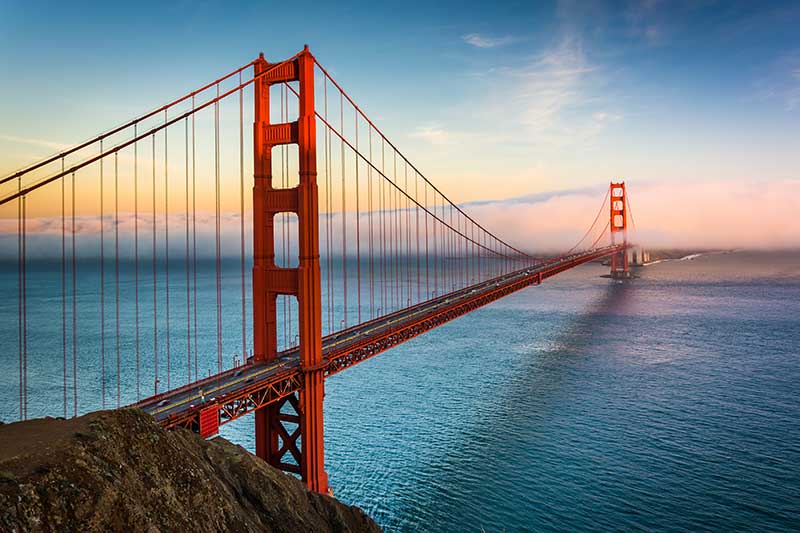 Aerial view of the Golden Gate Bridge, showcasing its iconic orange-red color against the blue water and skyline.